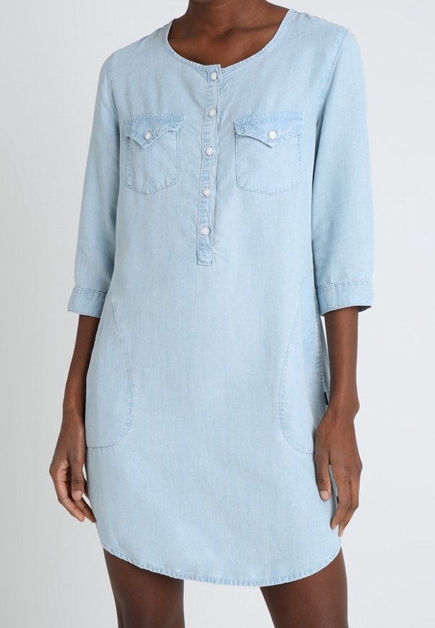 Femme portant une robe en jean bleu clair avec manches trois-quarts, patte de boutonnage devant et poches à rabat poitrine.
