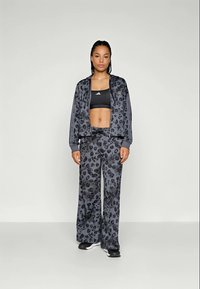 Conjunto atlético em estampa de leopardo cinza, composto por uma jaqueta cropped com fecho éclair e calças largas, combinado com um sutiã desportivo preto e sapatilhas.