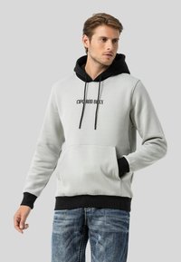 Hellgrauer Hoodie mit schwarzen Akzenten und Kordeln, ausgestattet mit einer vorderen Kängurutasche und bedrucktem Schriftzug auf der Brust.