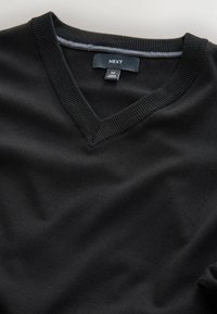 Schwarzer Pullover mit V-Ausschnitt, geripptem Kragen und weicher Textur. Das Etikett trägt die Aufschrift "NEXT", Größe M, hergestellt in Kambodscha.