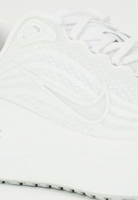 Gros plan d'une basket blanche Nike montrant un tissu texturé, des lacets et le logo Nike swoosh sur le côté de la semelle.