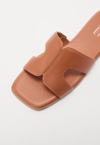 Sandale mule en cuir marron avec un bout carré et une large bride asymétrique sur le dessus du pied.