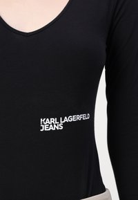 Black long-sleeve top made of soft fabric, featuring a V-neckline and white text "KARL LAGERFELD JEANS" on the left side.