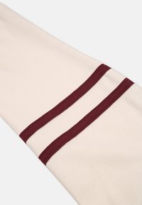 Tessuto color crema con bordi bordeaux, caratterizzato da due strisce orizzontali. La trama appare morbida e liscia, adatta per un abbigliamento informale.