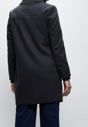 Mörkgrå ullrock med hög krage, ribbade ärmslut och rak silhuett, med sömlös axeldetalj och slät yta.