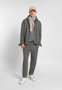 Grå texturerad jacka med matchande byxor, ljusgrå scarf och beige keps. Outfitten har en enkel design och avslappnade sneakers.