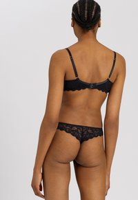 Svart spetsunderkläder i set med en scalloped design, justerbara axelband och ett hyska-och-ögla-stängning, som visar ett delikat blommönster.