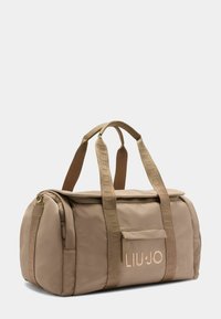 Borsa a mano in nylon beige con doppio manico superiore e dettagli con logo. Caratterizzata da una chiusura con zip e una tasca frontale per ulteriore spazio di archiviazione.