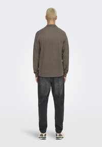 Bruin langemouw shirt met een klassieke kraag, gecombineerd met donkerdenim broek en sneakers met groene accenten, gezien vanuit de achterkant.