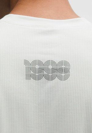 Bílá texturovaná košile s šedým kruhovým vzorem a číslem „1998“ potisknutým na zádech.