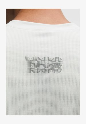 Bílá texturovaná košile s šedým kruhovým vzorem a číslem „1998“ potisknutým na zádech.