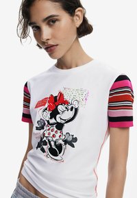 White cotton short-sleeve t-shirt featuring a Minnie Mouse graphic, polka dot dress, and multicolored striped ribbed sleeves.