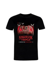 Camiseta de algodón negra con un diseño gráfico de una criatura monstruosa y murciélagos, con texto en rojo y blanco que dice "Stranger Things" y "¿Entrar al Mundo del Revés?"