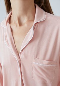 Ljust rosa pyjamasöverdel med klassisk krage, vit passpoal och en liten bröstficka. Mjuk tyg med en slät yta.