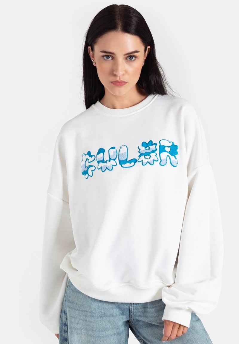 Biała, przesadnie duża bluza z okrągłym dekoltem, z niebieskim graficznym napisem "COLOR" w kwiatowym stylu. Miękka tkanina i ściągacze przy rękawach.