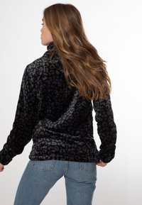 Pullover con stampa leopardata nera realizzato in tessuto morbido e texturizzato. Presenta un colletto alto e maniche lunghe. Abbinato a jeans di denim blu chiaro.