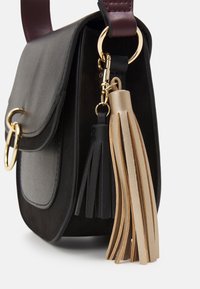 Borsa in pelle nera e grigia con forma arrotondata, dotata di un tassel rimovibile con accenti dorati in nero e beige, e una tracolla color borgogna.