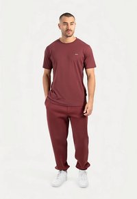 Bordeauxkleurig katoenen T-shirt met korte mouwen en een ronde hals, gecombineerd met bijpassende bordeauxkleurige joggingbroek en witte sneakers.