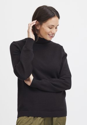 Pull à col roulé noir en tissu doux, avec des manches et un ourlet côtelés, associé à un bas vert olive.