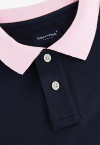Polo marine avec un col rose clair, deux boutons blancs et une étiquette Eden Park Paris à l'intérieur du col.