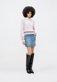 Suéter de canalé rosa claro con cuello blanco, combinado con una mini falda vaquera azul con botones al frente y botas negras hasta la rodilla.