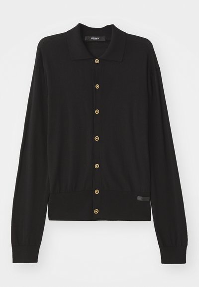 Must mustrõiv, mis on valmistatud pehmest kudumisest, sisaldab kraega dekolteed, pikki varrukaid ja kuldseid nööpe esiosal.