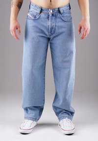 Light blue denim jeans with a relaxed fit, featuring five pockets, contrast stitching, and a button closure. Paired with white sneakers.