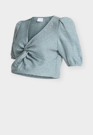 Blouse courte bleu clair avec manches courtes bouffantes et détail torsadé à l'avant, en tissu texturé.