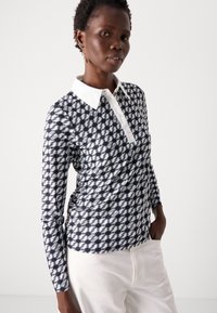 Langarm polo-shirt in marineblauw en wit, met een geometrisch patroon, knoopsluiting en een contrasterende witte kraag. Gladde stofstructuur.