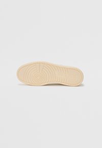 Semelle en caoutchouc beige clair avec un motif de bande de roulement circulaire et une marque en relief. Texture lisse avec une légère flexibilité, conçue pour le confort et l'adhérence.