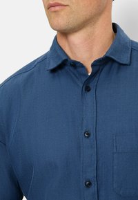 Hemd in marineblauem Fischgrätmuster mit Button-Down-Kragen, ausgestattet mit schwarzen Knöpfen und einer einzelnen Brusttasche. Weicher Stoffstruktur.