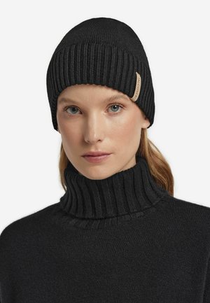 Sort ribbet strikket hue med en læderlogo-indsats, parret med en matchende sort ribbet højhalset sweater; blød tekstur og tætsiddende design.