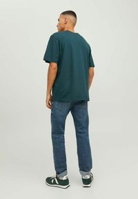 Camiseta de algodón color teal, corte relajado, mangas cortas; combinada con jeans de mezclilla azul y zapatillas verdes con acentos blancos y logotipo.