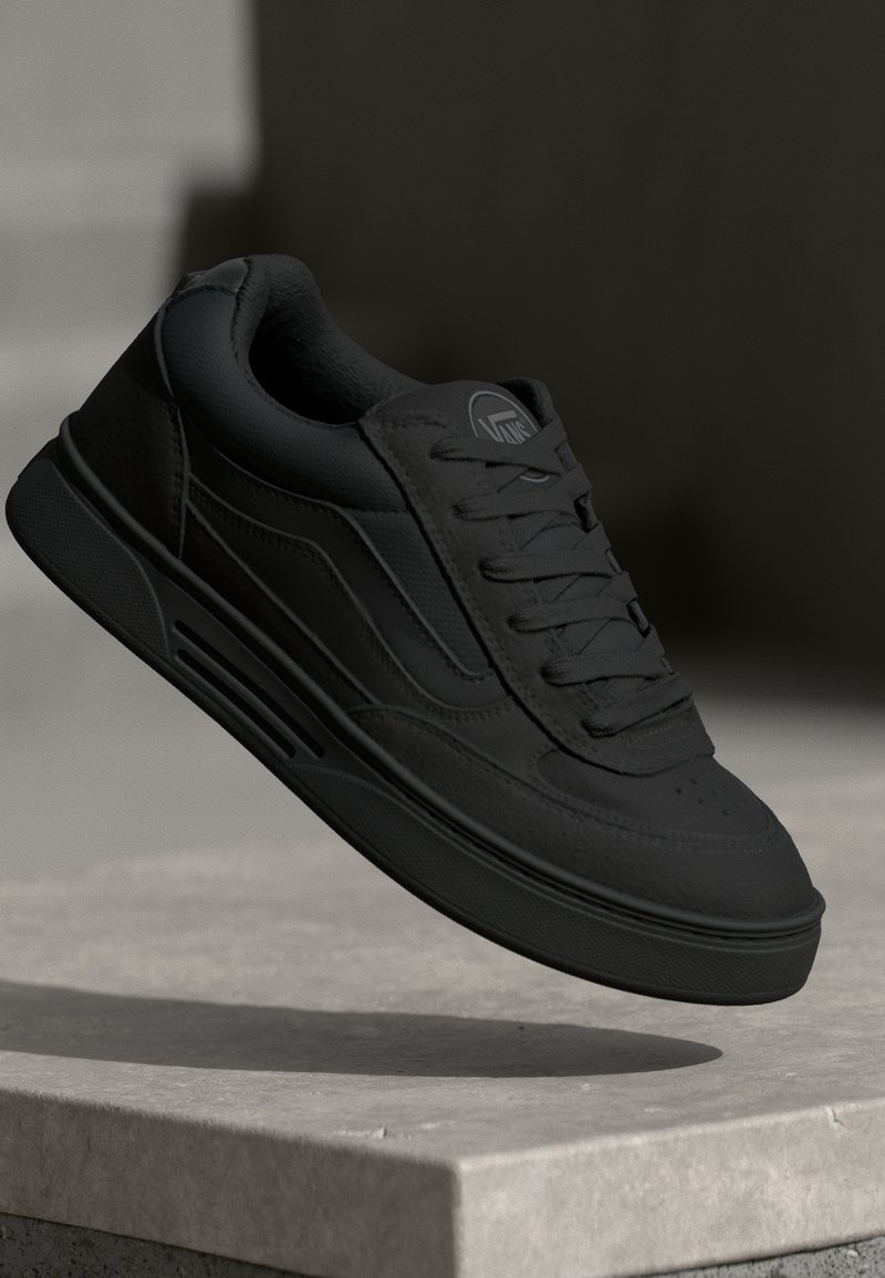 Zwarte sneaker met een bovenwerk van glad leer, ronde neus, platte vetersluiting en een gestructureerde buitenzool. Bevat minimaal merk en zijdetails.