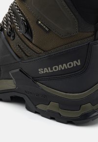 Buty trekkingowe Salomon w ciemnozielonym i czarnym kolorze, z teksturowaną cholewką, etykietą Gore-Tex, wzmocnionym noskiem oraz solidną podeszwą zapewniającą przyczepność.