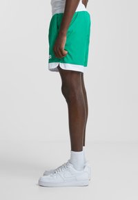 Grønne sports-shorts med hvid trim, der fremhæver et let stof, elastisk talje og kontrastlogo-detalje på forsiden.