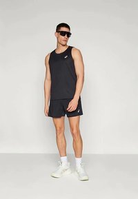 Black athletic tank top and shorts, made of lightweight material, featuring a minimal logo. White sneakers and dark sunglasses complete the look.