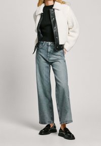 Faux shearling and leather jacket, black sweater, light-wash wide-leg jeans, black loafers with gold detailing, casual outfit design.