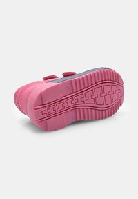 Růžová dětská teniska s texturovanou gumovou podrážkou a dvojitými suchými zipy, zobrazená ze spodní strany na bílém pozadí.