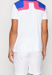 Herrens träningsskjorta med vit bas, blå och rosa axeldetaljer, korta ärmar och rundad halsringning.