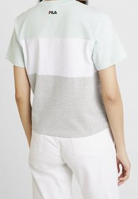 Camiseta de manga corta con bloques de color horizontal en aguamarina claro, blanco y gris, con un pequeño logo de FILA en negro en la parte trasera del cuello.