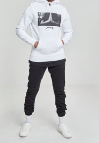 Witte hoodie met een grafisch ontwerp van gevouwen handen en het woord "bid", gecombineerd met zwarte taps toelopende joggingsbroek en witte sneakers.