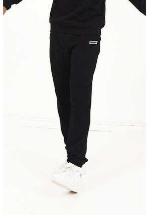 Sorte fleece joggerbukser med en tætsiddende design, ribbet manchet og et lille logo-patch på hoften, parret med hvide sneakers.
