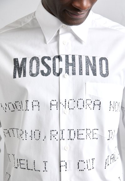 Cămașă albă cu butoni, având un text negru îndrăzneț "MOSCHINO" și modele de text punctat, cu guler clasic și un buzunar pe piept.