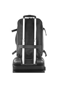 Mochila negra con superficie texturizada, correas ajustables integradas y mango telescópico metálico plateado sobre una maleta rígida negra.