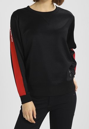 Sweatshirt noir avec des bandes rouges sur les côtés, col rond et manches longues. Fabriqué dans un tissu doux avec une coupe décontractée. Design minimaliste.