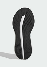 Semelle d'une basket noire et blanche avec un motif de bande de roulement texturé, vue du dessous sur un fond clair.