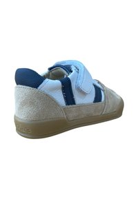 Zapatilla con un inferior de ante beige y un superior de cuero blanco, presenta acentos azules y una correa de Velcro, terminada con una suela de goma.
