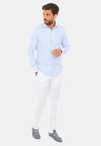 Camicia button-up a righe blu chiaro e bianche con maniche lunghe, abbinata a pantaloni bianchi e sneakers blu. Vestibilità casual, tessuto morbido.