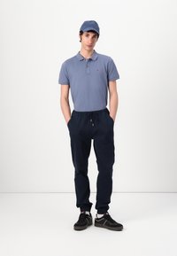 Light blue polo shirt and navy joggers. The joggers have an elastic waistband and side pockets. Black sneakers with white accents.